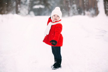 pretty little girl in red coat in winter forest. Little girl having fun on winter day. cheerful little baby girl in gloves and white hat runs on snow white