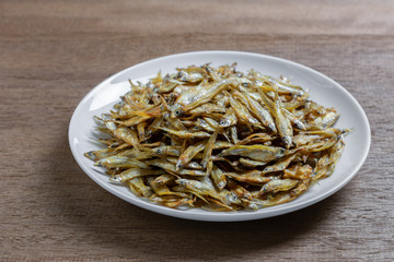 close up of roasted dried little fish with salt in a ceramic dish on wooden table. asian style food concept.