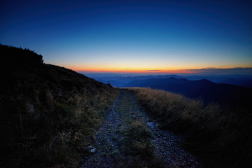 Beautiful sunrise over the mountain peaks and hills panorama, autumn rural landscape with dawn sky. Adventure mountain trekking. Moody light. Panoramic background