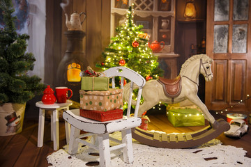 A lot of gifts in the New Year's interior. Christmas Eve. Cozy room with stove and rocking horse...