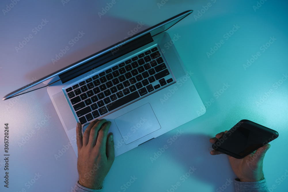 Aufkleber man working night online silver laptop and smart phone in the color light on a table night backgroun