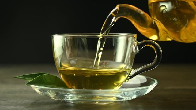 green tea is pouring from a teapot into glass cup