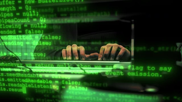 Green code characters running infront of typing haker's hands in a dark office room. Close-up shot. 4K (UHD)