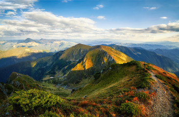 Fototapeta premium Hiking path in mountain peaks and hills panorama outdoor view, autumn rural landscape with cloudy sky. Adventure mountain trekking. Beautiful moody light. Panoramic background