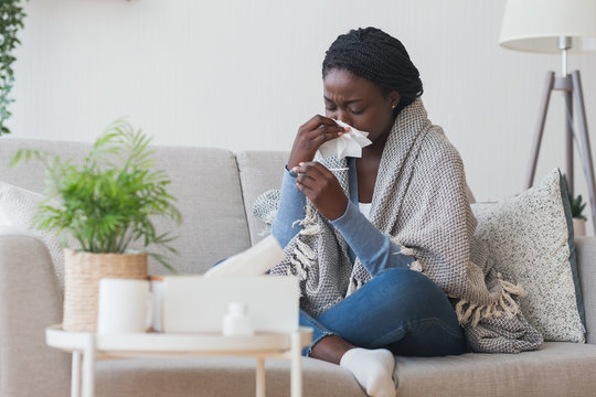 Black girl having flu, blowing nose and checking body temperature