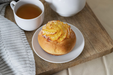 Grey blanket, wooden try with  tea and sweet bun on white sofa. Hygge Relax and stay at home concept.