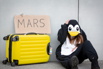 Young woman, with penguin costume and yellow suitcase, has to travel due to global warming....