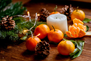 Fototapeta na wymiar tangerines, candle, lights, cones, tree branch on a wooden background