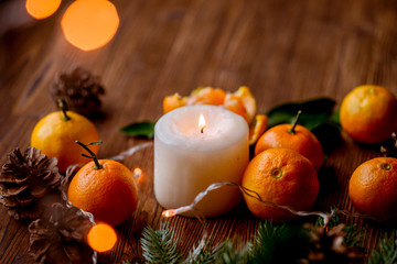 tangerines, candle, lights, cones, tree branch on a wooden background