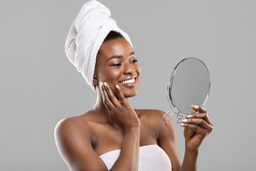 Beautiful african woman holding mirror and touching her perfect soft skin