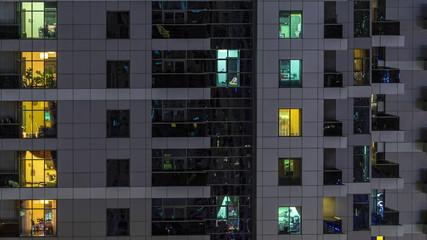 Rows of glowing windows with people in apartment building at night.