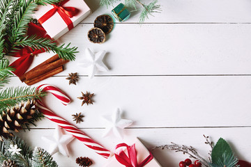 Beautiful Christmas composition on white background with golden Christmas gift boxes, snowy fir branches, conifer cones, holiday decoration and red berry. Top view