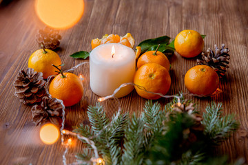 Fototapeta na wymiar Christmas and new year decor. Christmas card. Tangerines, candle, lights, cones on a wooden background