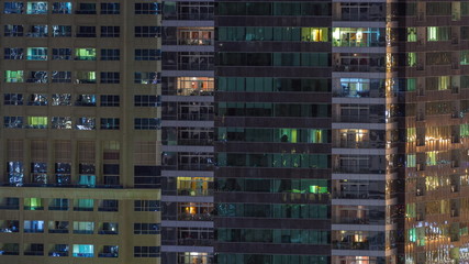 Rows of glowing windows with people in apartment building at night.