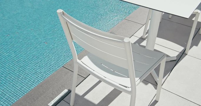 White chair and table is next to the blue water pool. Vacation concept. Summer season.