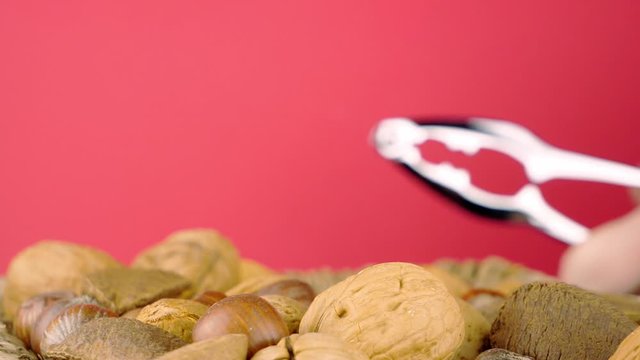 Behind a portion of mixed nuts, a brazil nut is cracked open using a metal tool