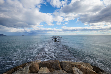 A pier of stones, a pier going into the sea. Dramatic sky with dark, heavy clouds.
