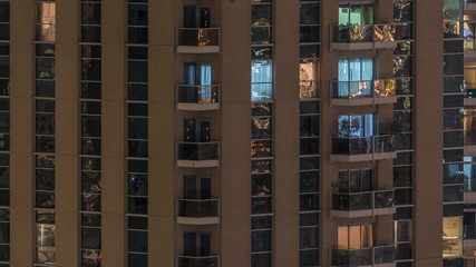 Rows of glowing windows with people in apartment building at night.