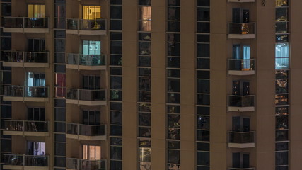 Rows of glowing windows with people in apartment building at night.