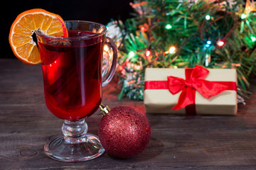 Christmas card. Glass cup with mulled wine, a slice of orange and spices on a dark wooden table.
