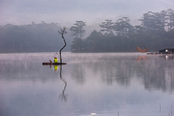 The old fishing man and small cabin with flooded trees reflection on the fog lake at sunrise
