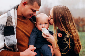 Artificial lactation bottle feeding. Mother and father feeding baby boy outdoor
