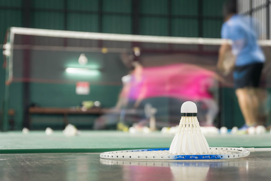 shuttlecock resting on a badminton racket with badminton player are competiting