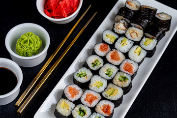 Sushi with fish, with cucumber, with eel, with avocado. Wrapped in Nori Seaweed. Food for vegetarians. Soy sauce, ginger, wasabi in white bowls. Copy space.