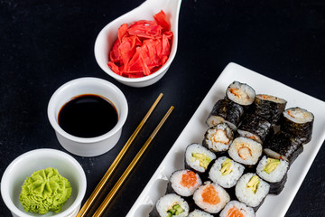 Sushi with fish, with cucumber, with eel, with avocado. Wrapped in Nori Seaweed. Food for vegetarians. Soy sauce, ginger, wasabi in white bowls. Copy space.