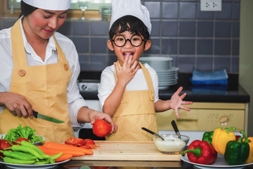  Asian woman young mother with son boy cooking salad mom sliced vegetables food son tasting salad dressing vegetable carrots and tomatoes bell peppers happy family cook lifestyle kitchen