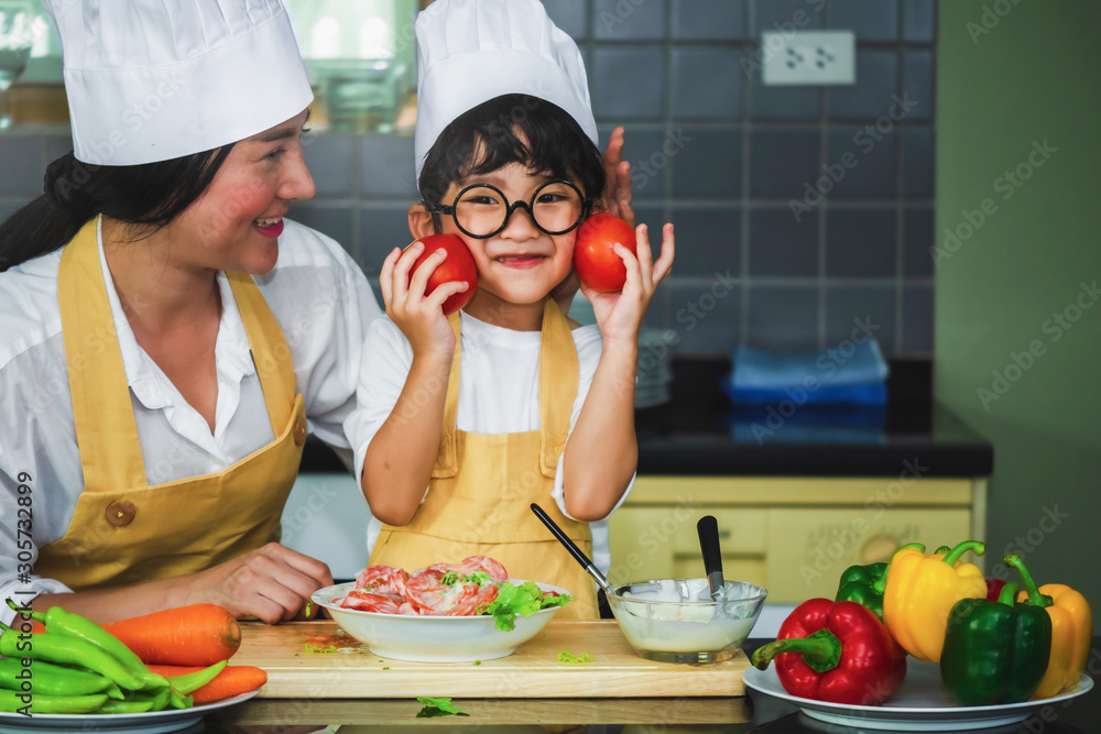 Poster  Asian woman young mother with son boy cooking salad mom sliced vegetables food son tasting salad dressing vegetable carrots and tomatoes bell peppers happy family cook food lifestyle kitchen