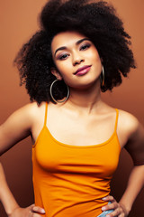 pretty young african american woman with curly hair posing cheerful gesturing on brown background, lifestyle people concept