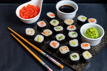 Sushi with fish, with cucumber, with eel, with avocado. Wrapped in Nori Seaweed. Food for vegetarians. Soy sauce, ginger, wasabi in white bowls. Copy space.