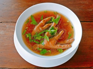 Chicken feet soup in white bowl on wooden table.