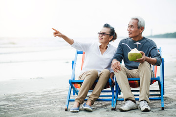 Romantic of senior couple sitting in deckchair on the beach together near sea and looking at the sea. Love is everything, Retirement age concept and love.