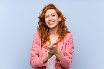 Redhead woman in suit over isolated blue wall applauding after presentation in a conference