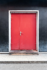 Obraz na płótnie Canvas Red door on a black wall background. The modern facade of the building. Urban concept.