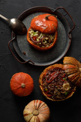 Healthy vegan food. Small pumpkins stuffed with red rice, mushrooms, leek, peppers, ptitim and raisins on vintage metal tray on black background