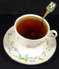 On the table on a black uniform background is a white porcelain Cup with tea, saucer and teaspoon with .