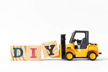 Toy forklift hold wood letter block Y to complete word DIY (Abbreviation of Do it yourself) on white background