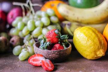 Photo of fresh strawberries with the strawberry leaf on rustic grey background. A bunch of ripe strawberries on the table with lemon grape kiwi banana. Copy space. Organic food. Clear food.