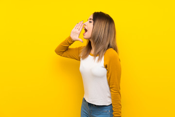 Pretty young woman over isolated yellow wall shouting with mouth wide open to the lateral