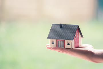 Obraz na płótnie Canvas Adult hand is holding red house model, outdoors. Concept for new home, property and estate