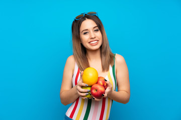 Young woman in summer holidays over blue background holding fruits