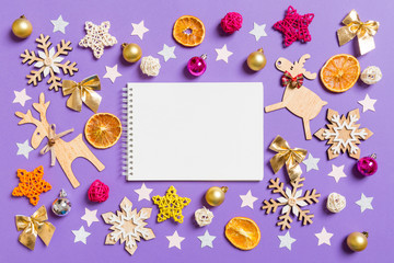 Naklejka na ściany i meble Top view of notebook surrounded with New Year toys and decorations on purple background. Christmas time concept