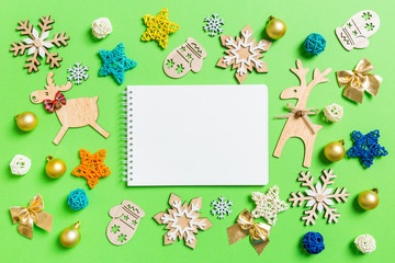 Fototapeta premium Top view of notebook on green background with New Year toys and decorations. Christmas time concept