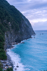 Aerial view of rocky mountainous coast with green trees and blue sea blue sky with white foaming waves