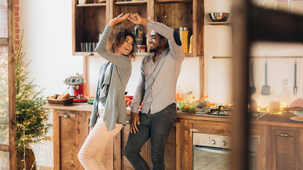 Young african-american couple dancing in kitchen, copy space
