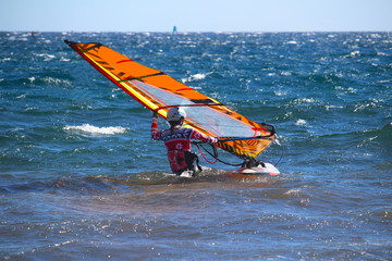 Female windsurfer preparing board and sail position for beachstart (El Medano, Spain)