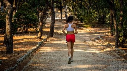 Teen in red shorts and white tanktop jogging on dirt trail from the back